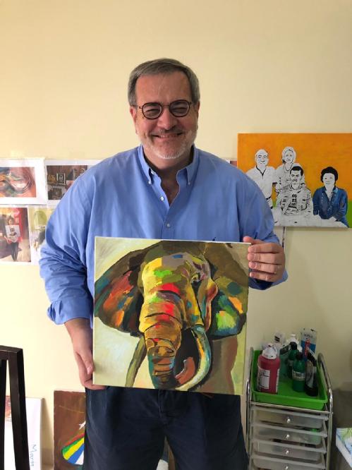 David smiles wearing glasses and holds up a painting of an elephant