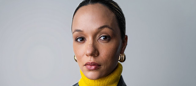 Georgina looks to camera wearing a yellow polo neck