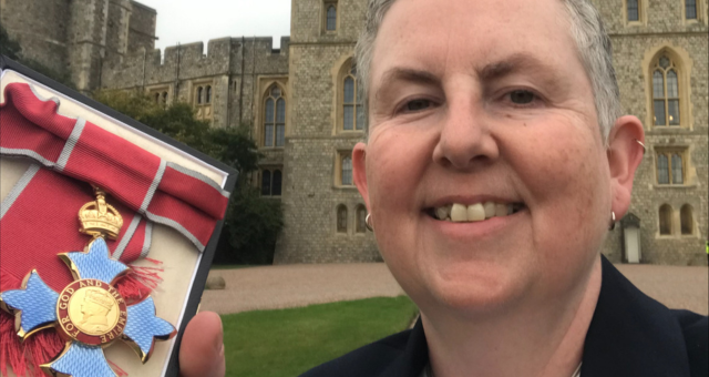 Jo Todd smiles at camera holding up her MBE