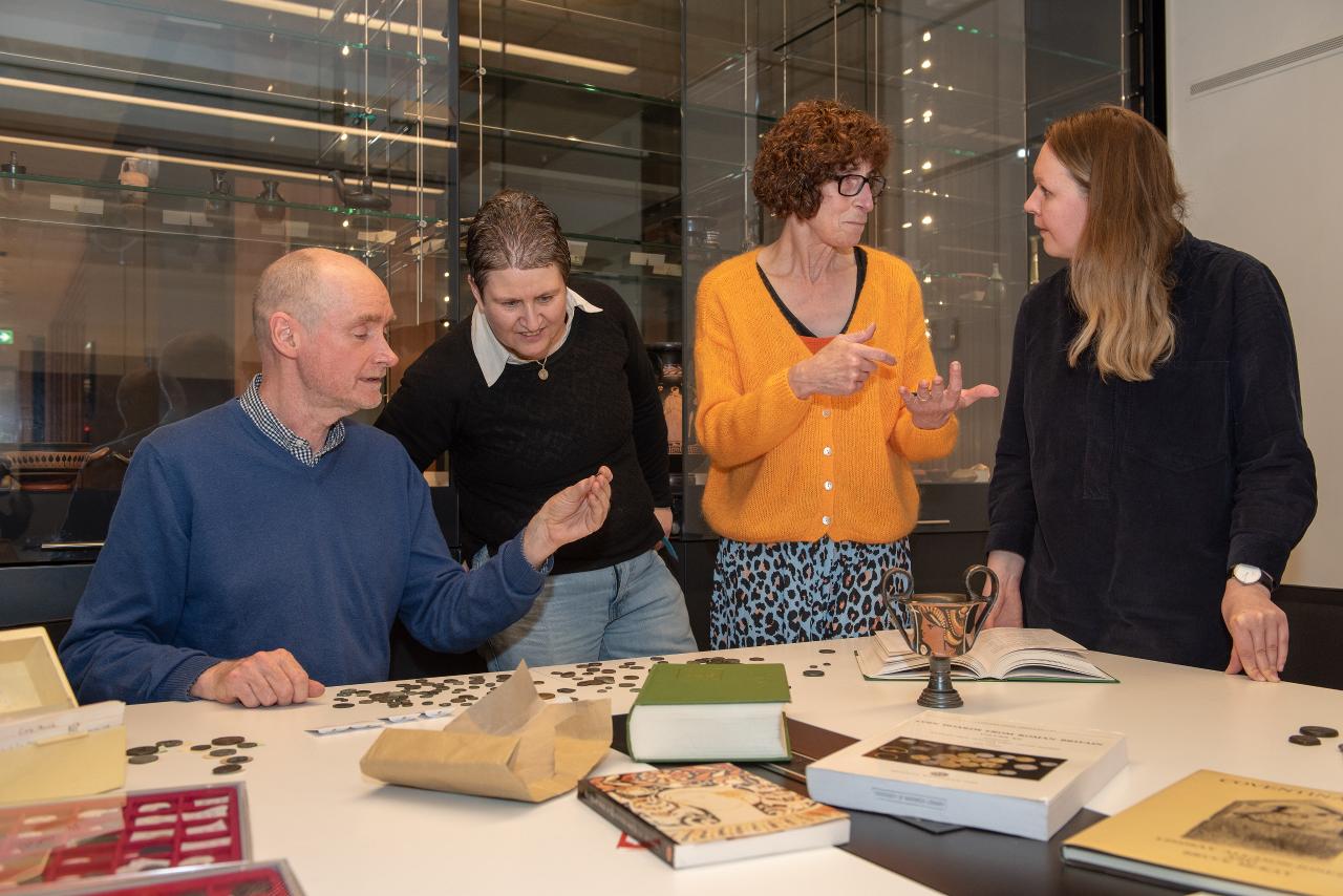 Image of four people looking closely at coins (Prof. Kevin Butcher, Sue Walker, Prof. Suzanne Frey-Kupper and Dr Naomi Carless-Unwin)