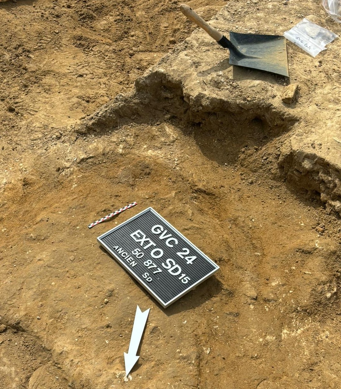 An archaeological photo board and north arrow placed for photography on a background of soil.