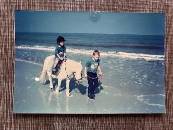 Sam is sat on a horse, while Dan leads the horse, they are both in the sea.