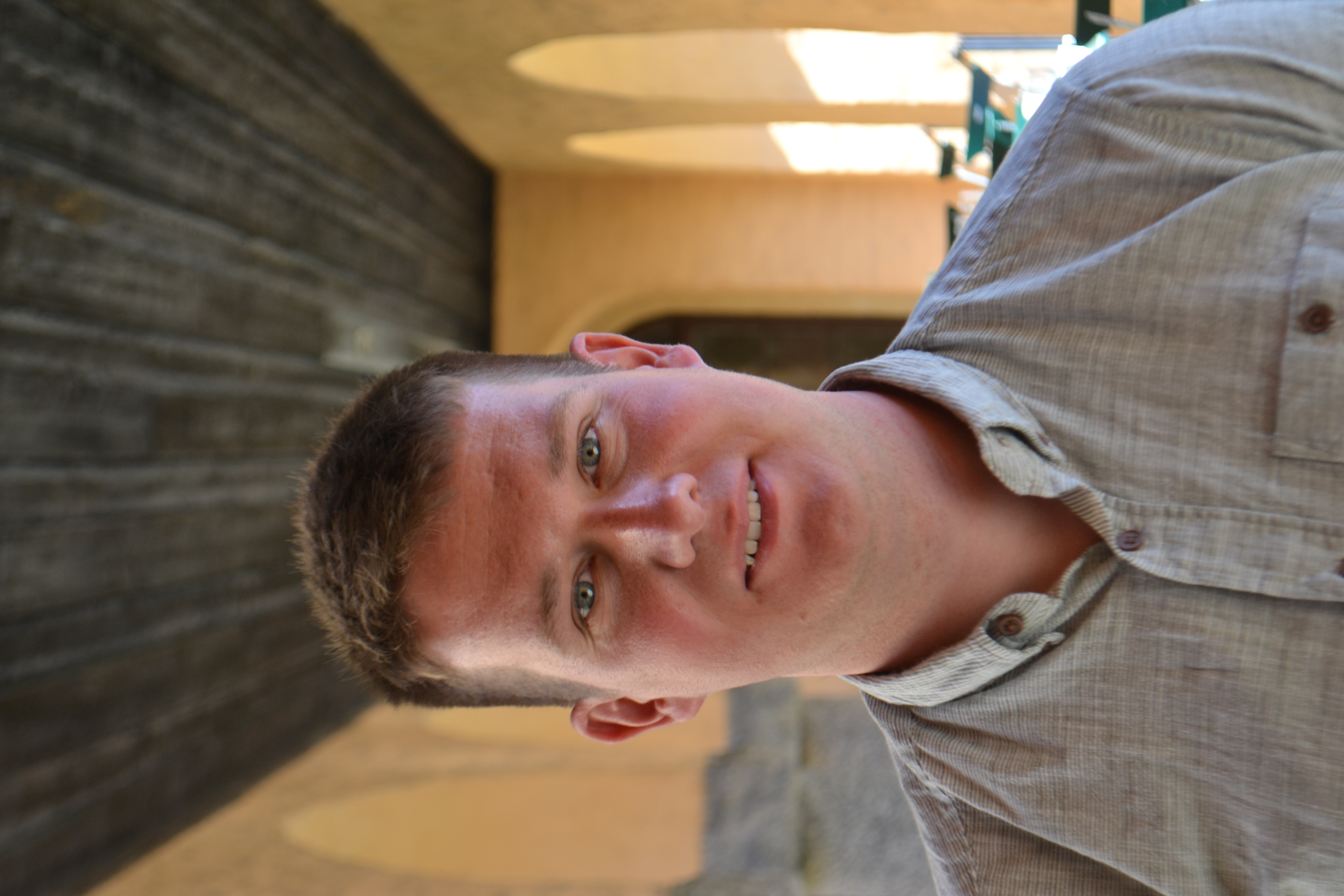 Photograph of Andrew Burchell taken against backdrop of orange painted cloisters and green patio furniture.