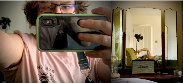 two photos. the first shows the subject taking a selfie, most of their face is obscured by a phone. they are wearing a light pink tshirt that says Bee Kind with a bee drawn on it, they have metal glasses and short messy brown hair.  The second photo shows a three peice mirror in a dressing table, in the mirror we can see the subject in bed, mostly obscured except an arm arched over their head with a theatre studio light in the background.