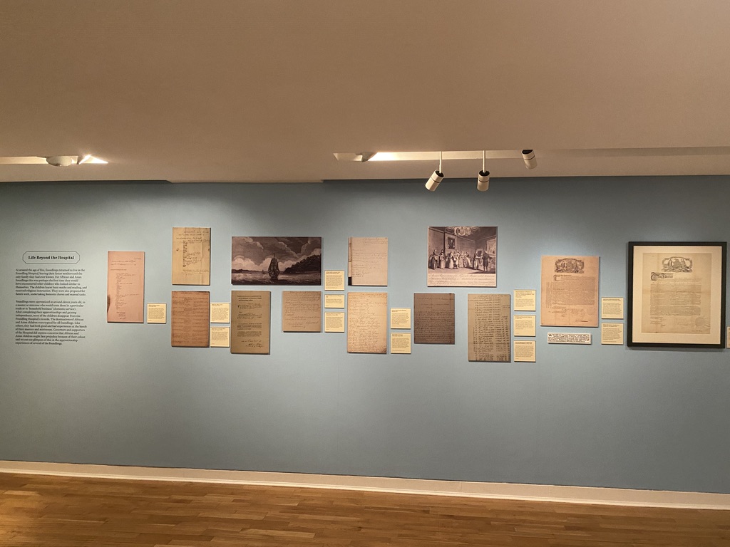 Various documents and labels displayed on a blue wall in an exhibition
