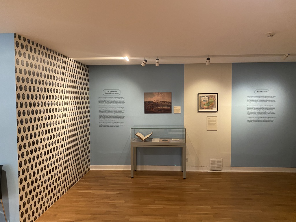 Exhibition gallery showing wall text, two pictures and a display case