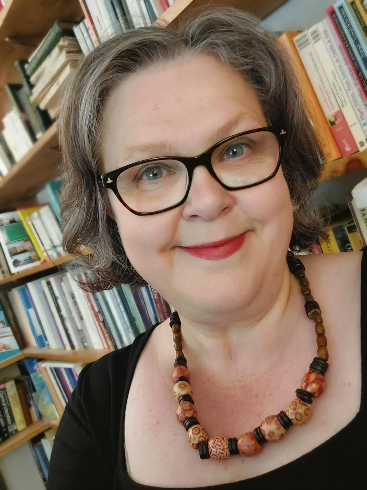 Headshot of Professor Hooper wearing black and standing in front of a bookcase like a proper academic