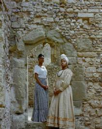 Two Black women in 18th-century clothing standing in a stone castle