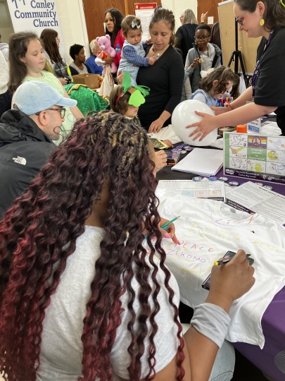 people of a variety of ages adding multilingual messages about peace to blank t-shirts with fabric pens