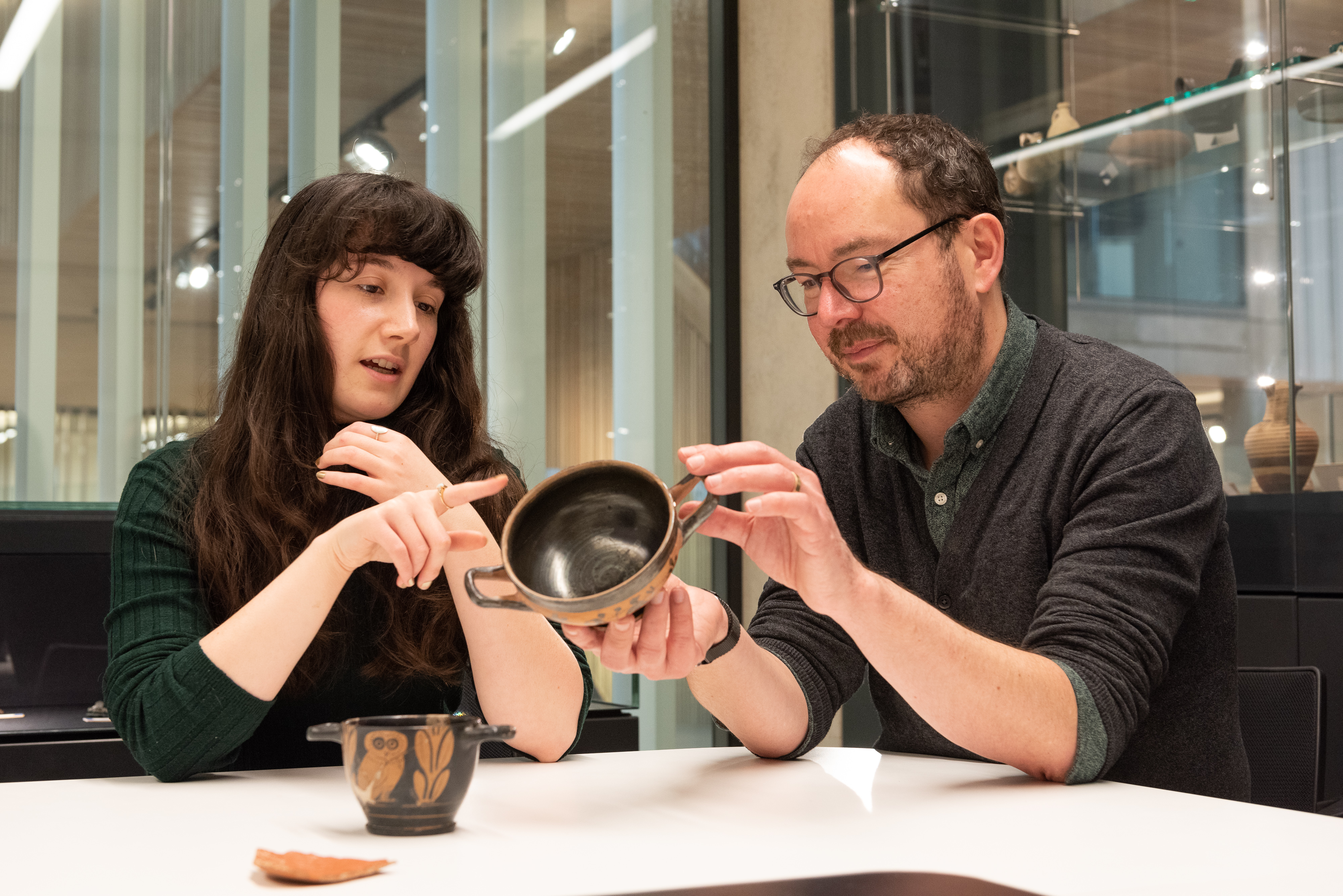 Staff Member holding a classical pottery artefact and discussing with university student
