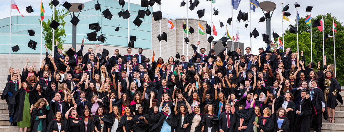 A large group of University of Warwick alumni throwing their caps into the air in celebration.