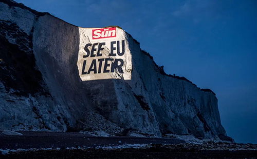 The image depicts a video projection onto a cliff face at Dover, which reads "The Sun. SEE EU LATER"