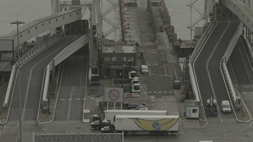 A view down into port area. Ramps lead up from a tarmac area in which a lorry with a large banana graphic is stationed. 