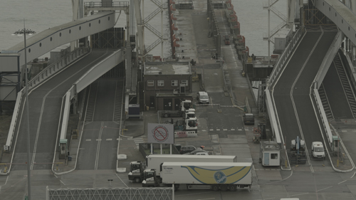 A view down into port area. Ramps lead up from a tarmac area in which a lorry with a large banana graphic is stationed. 