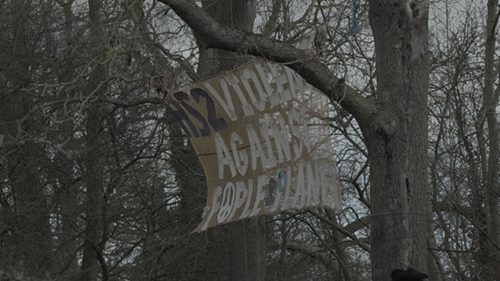 A large banner suspended between trees reads: "HS2 VIOLENCE AGAINST PEOPLE & PLANET"