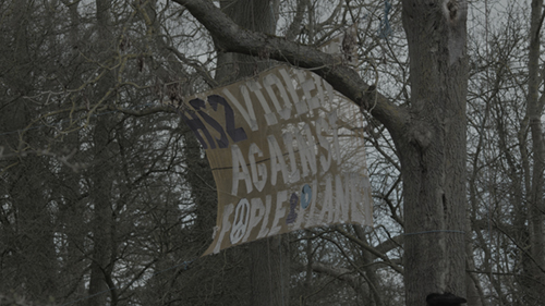 A large banner suspended between trees reads: "HS2 VIOLENCE AGAINST PEOPLE & PLANET"