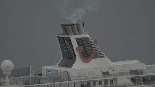A cruise ship belches steam from its exhaust funnel, against a grey background.