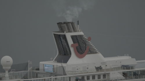 A cruise ship belches steam from its exhaust funnel, against a grey background.