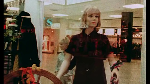 Image depicting a woman browsing in a shopping mall. There are mannequins in a shop window.