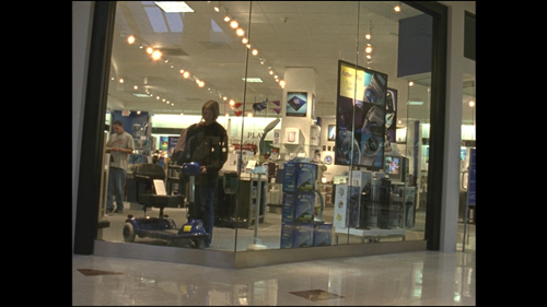 Image depicting a woman browsing in a shopping mall, inside a shop. The mall lights create reflections in the shop window.