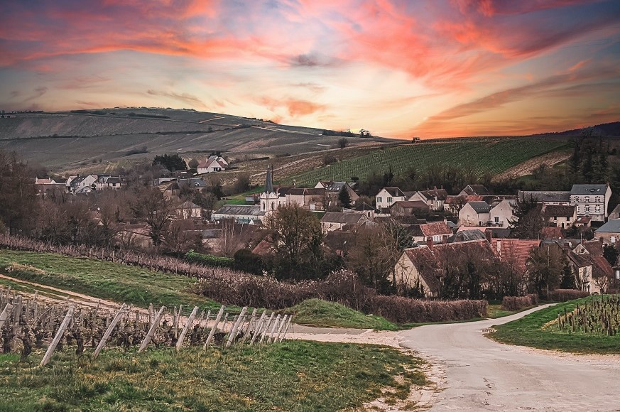 A rural location with rolling hills, thatched houses, and a colourful red sky