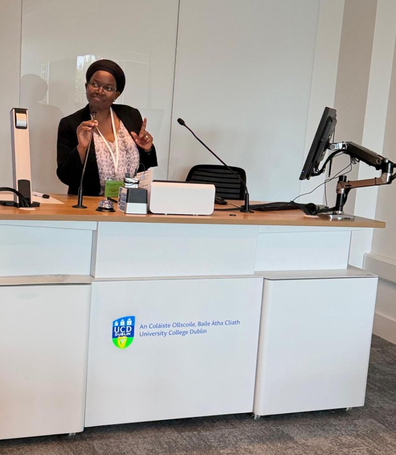 Hadijah holds microphone as she stands behind a desk ready to give her presentation