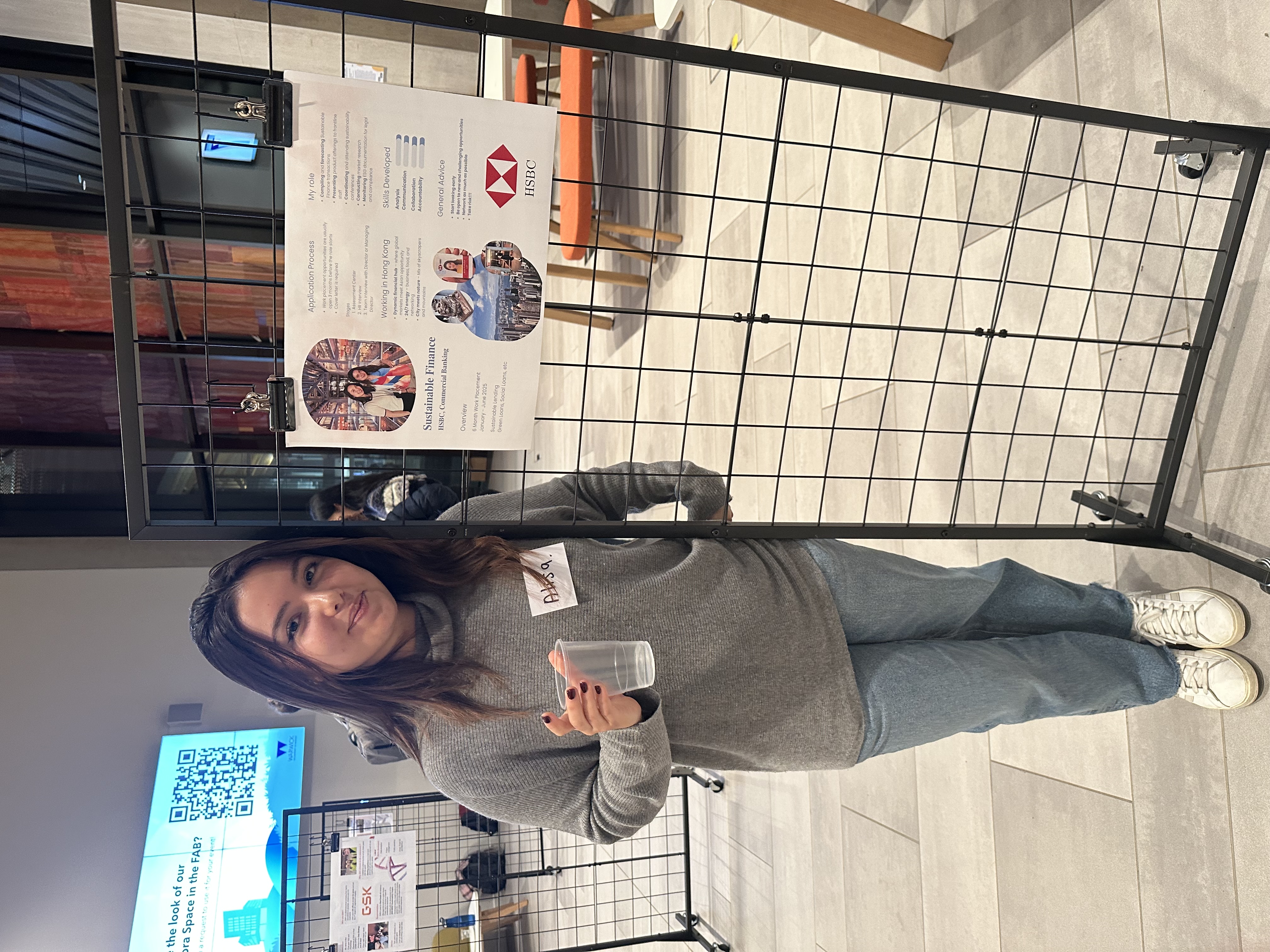 Alisa smiles at camera whilst standing in front of her presentation poster at the Work Placement Fair 2025