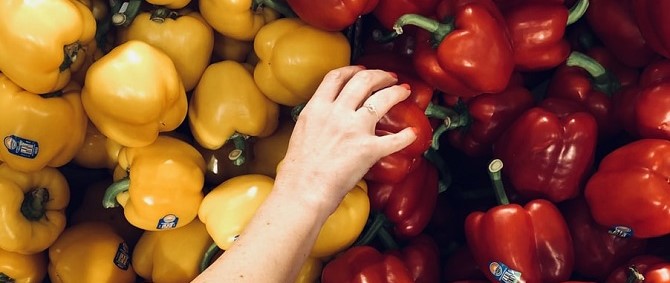 Vegetables, specifically red and yellow peppers, with a hand reaching for one