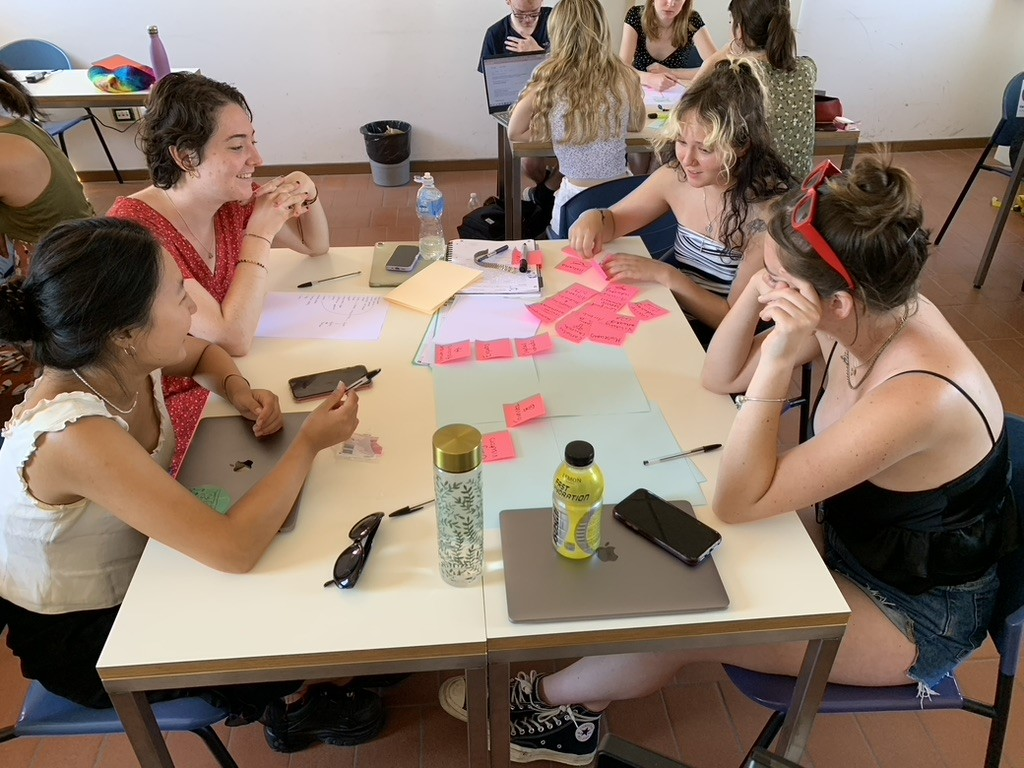 A group of students in a classroom, sat around a table brainstorming with post-it notes