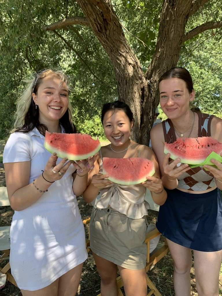 Students standing in the shade under a tree eating watermelon