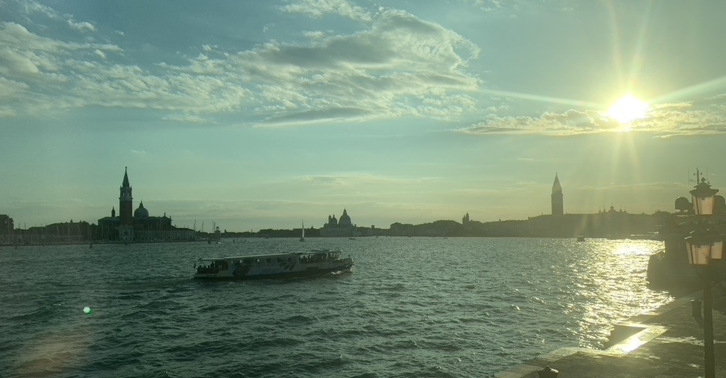 Venice skyline. The sun is shining onto the water, with a boat passing by.