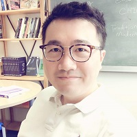 A headshot of Dr Xiaodong Lin. Dr Lin is smiling, sat in a classroom with a blackboard and bookshelf in the background.