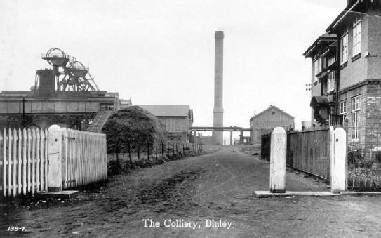 Historic photograph of the Binley Colliery showing the entrance gates (foreground), winding gear (left), and chimney (rear)