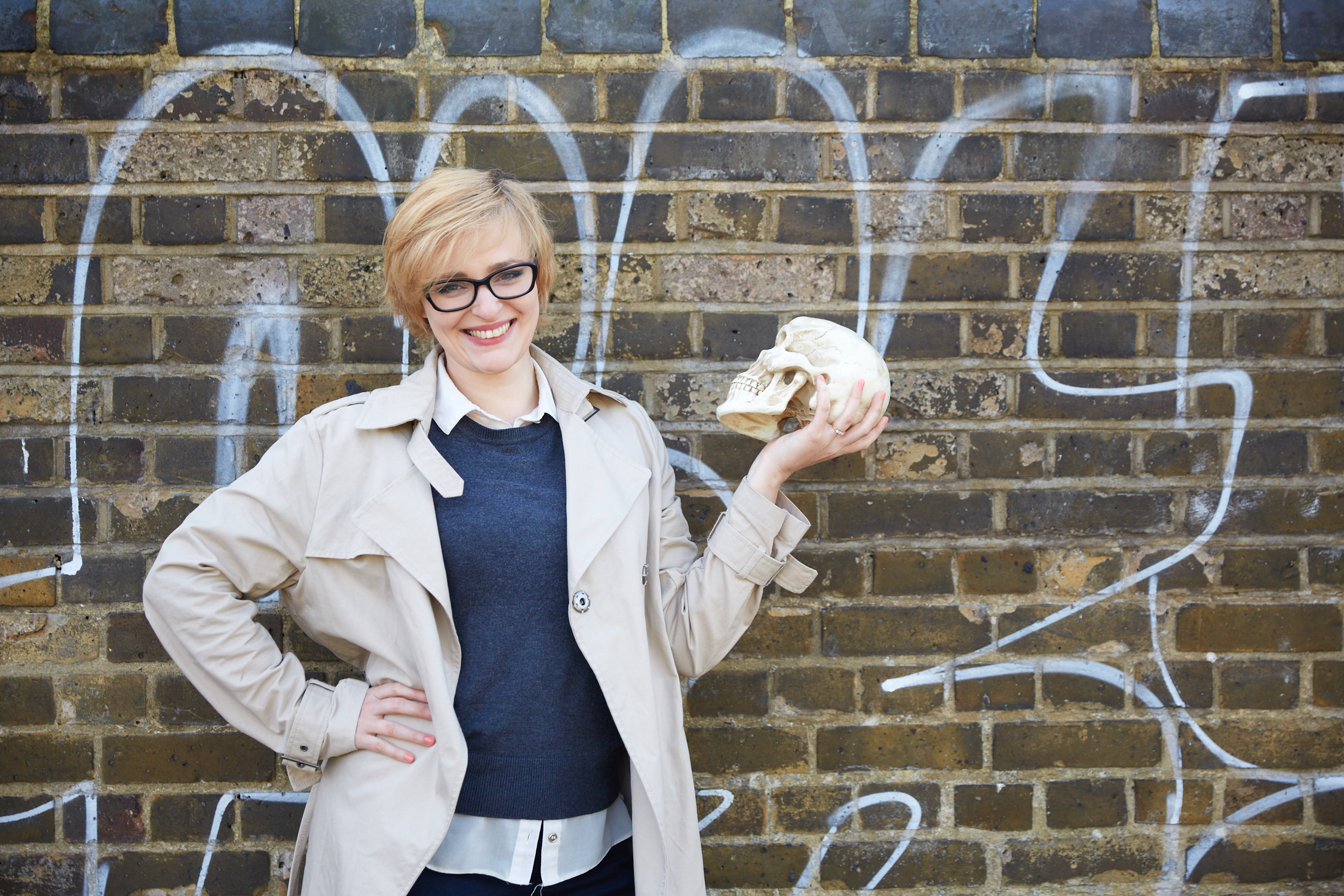 headshot of Jennifer Kitchen holding a toy skull in front of a graffiti-ed brick backdrop