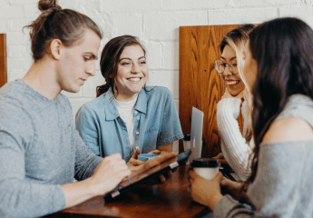 Four students smiling around a table having a meeting