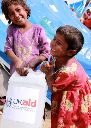 Children smile as they carry a bottle of detergent supplied by UKaid from the British government, as part of the UK