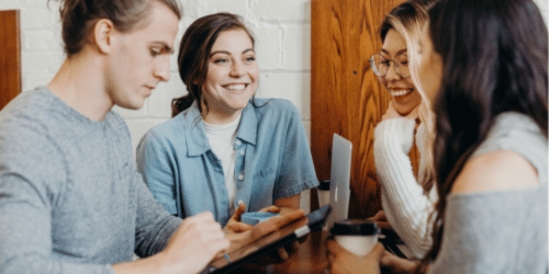Four students smiling around a table having a meeting