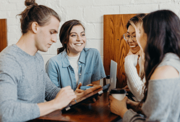 Four students smiling around a table having a meeting