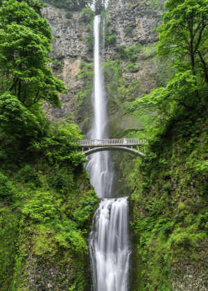 waterfall down a mountain with a grey bridge