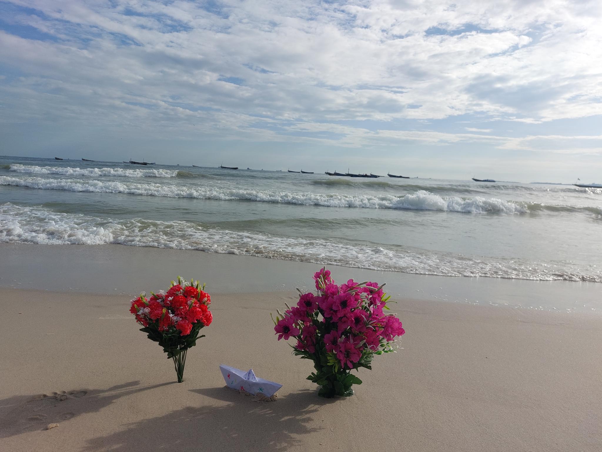 Red and pink flowers on a beach with a small paper boat