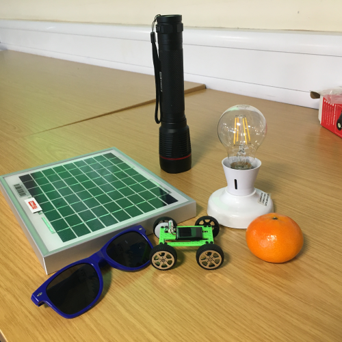 a display of a solar panel, sunglasses, torch, lightbulb, satsuma and a solar powered toy car