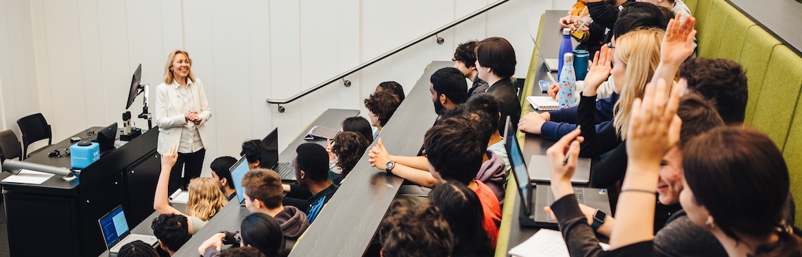 Students in a lecture, with a lecturer standing at the front of the room.