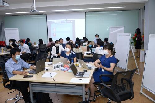 A group of staff attend a training session, all are wearing masks, they sit in small groups discussing content