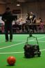 A non-standard platform robocup player chases a runaway ball as the operator looks on in the background.
