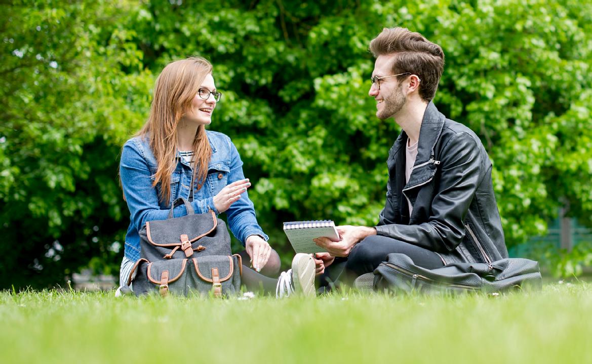 A female and a male student sitting on the grass at Gibbet Hill