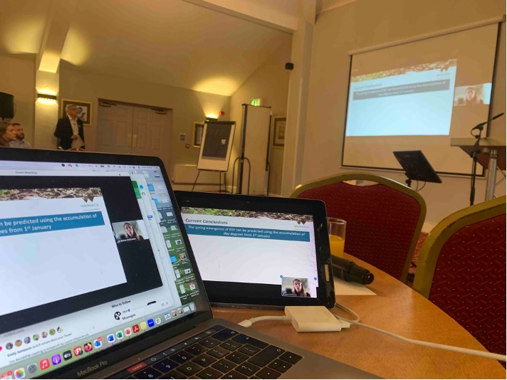 Image shows two computers and large screen with Becca McGowan presenting her work remotely