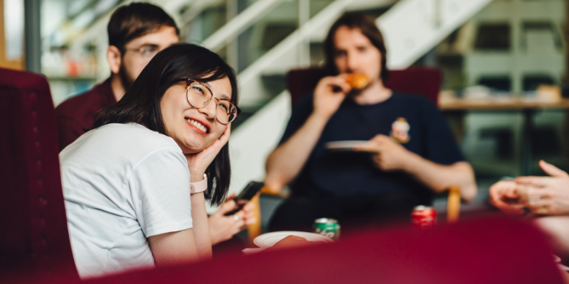 A female student smiling with two male students out of focus in the background