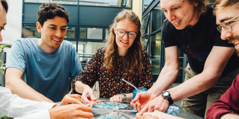 A group of staff and students gathered at a small table examining some mathematical models