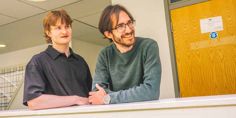 Two male students leaning on a balcony and laughing