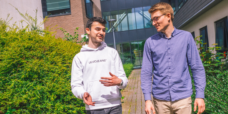 Two male students walking and talking outside a university building